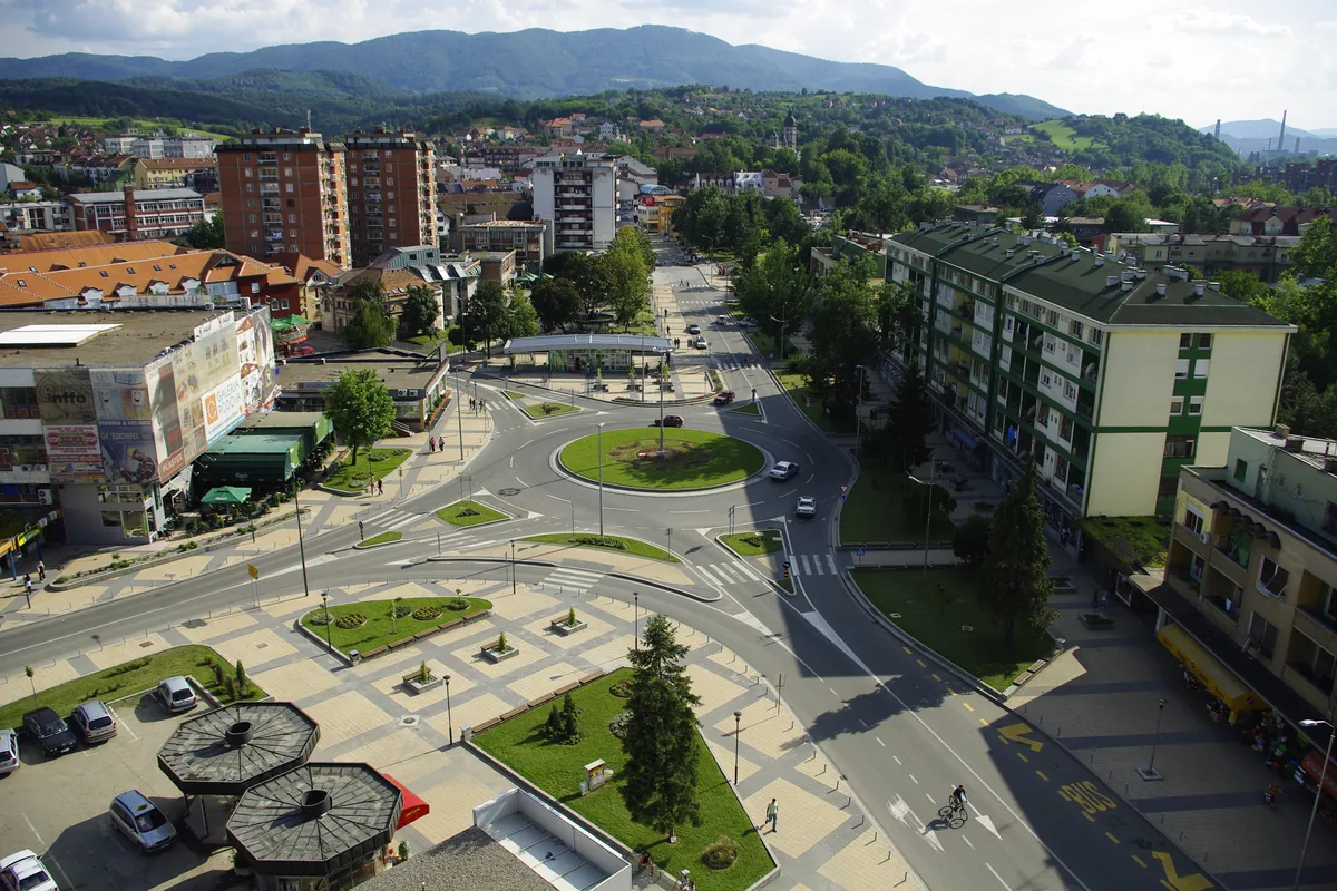 Pogled odozgo na Trg Vuka Karadžića u Loznici sa kružnim tokom, zelenilom i stambenim zgradama, planine u pozadini