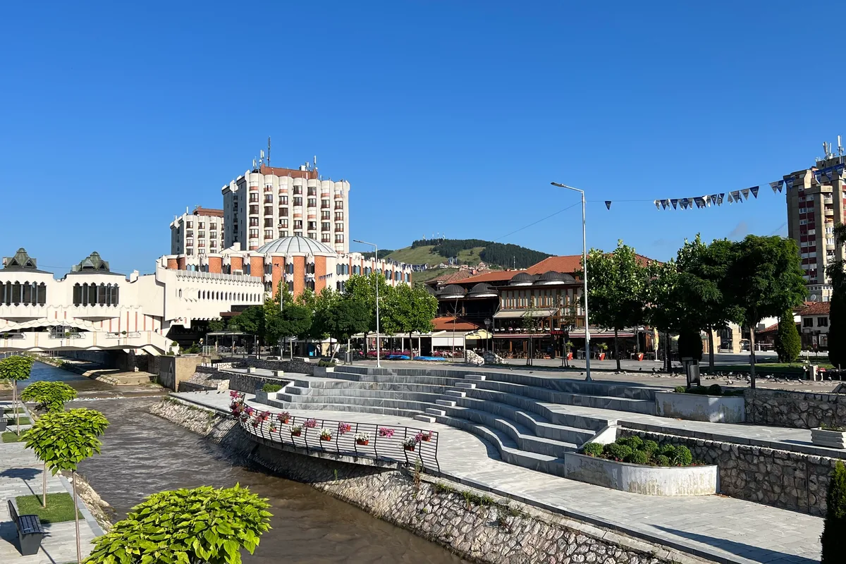 Uređeno šetalište i stepenice uz reku u Novom Pazaru, hotel i zgrade u pozadini, vedar letnji dan