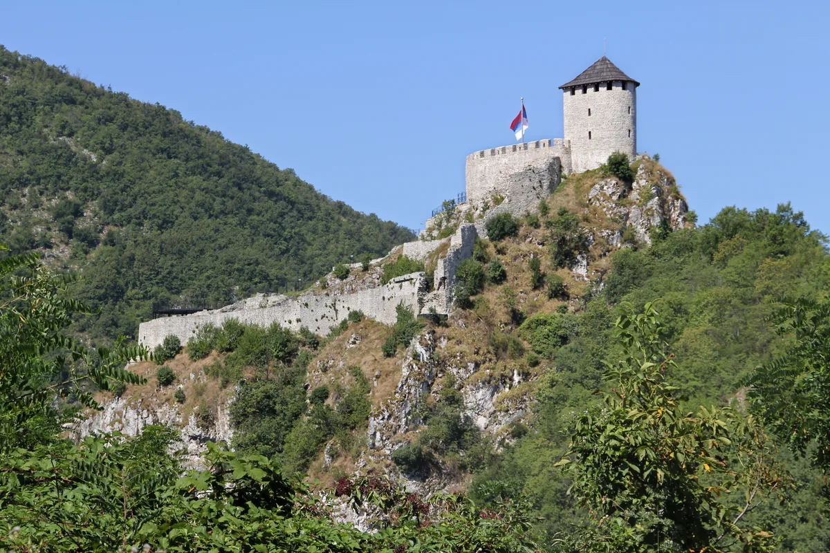 Kamena kula i bedemi tvrđave Užički grad na stenovitom brdu obraslom šumom, vedro nebo