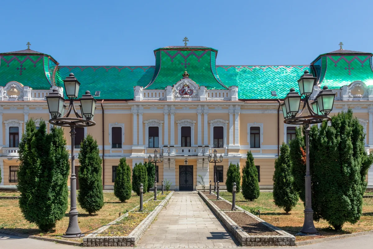 Vladičanski dvor u Vršcu sa zelenim krovom, ulazna staza između čempresa i ukrasnih svetiljki